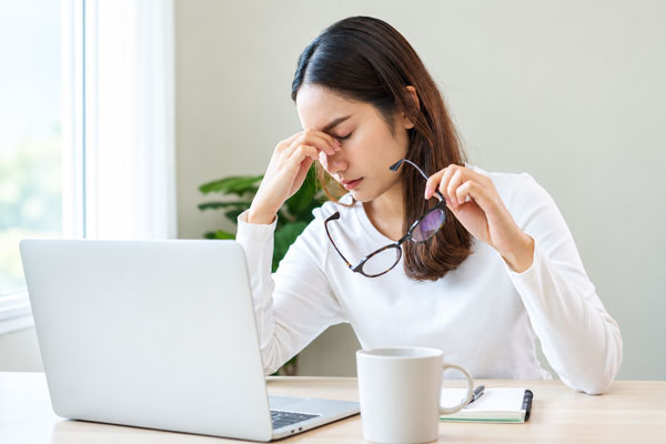 Woman holding glasses and rubbing her eyes beside a laptop